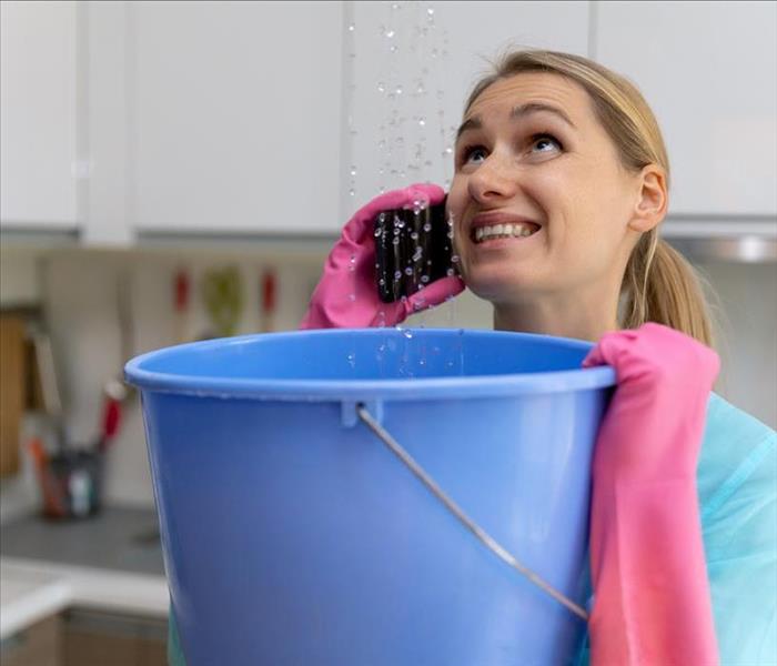 woman holding bucket under ceiling leak